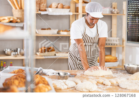 Caucasian guy works in bakery as baker, kneads dough, works with flour. 128067168
