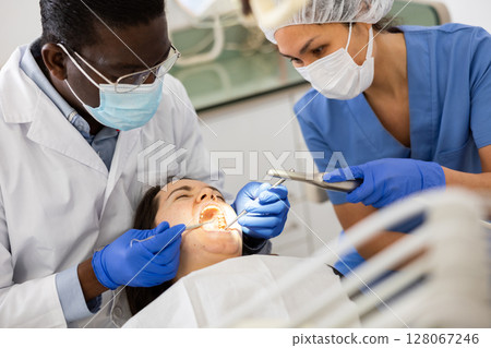 Professional dentist with female assistant performing teeth treatment to woman 128067246