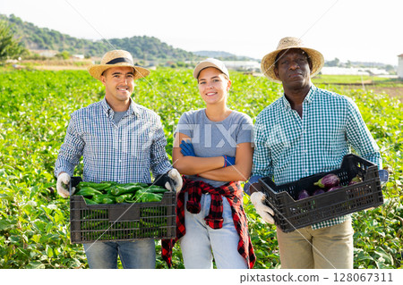 Cheerful farmers standing in field with harvested peppers and eggplants 128067311