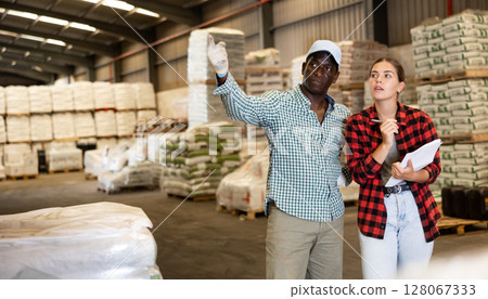 Man talking with young woman in warehouse and pointing with his hand at boxes of products Man talking with young woman in warehouse and pointing with his hand at boxes of products 128067333
