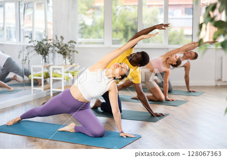 Asian woman practicing Parighasana during group yoga session Asian woman practicing Parighasana during group yoga session 128067363