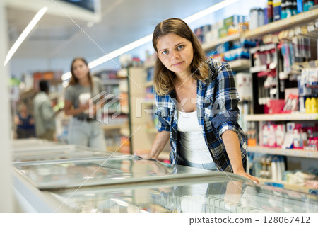 Woman standing at refrigerator in supermarket, choosing frozen food 128067412
