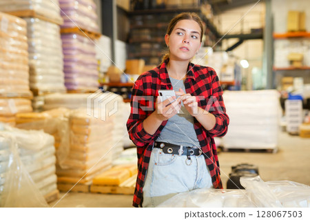 Young woman warehouse worker using smartphone in her work 128067503