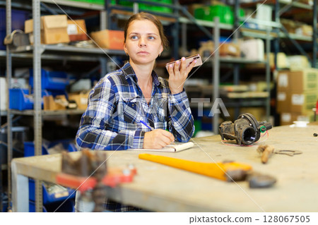 Female worker takes an order on a mobile phone and makes notes in notebook 128067505