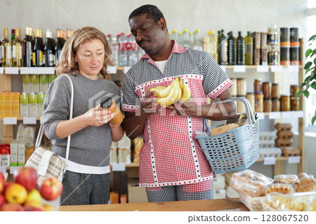 Married couple with various products in hands continuing shopping in grocery department of supermarket 128067520