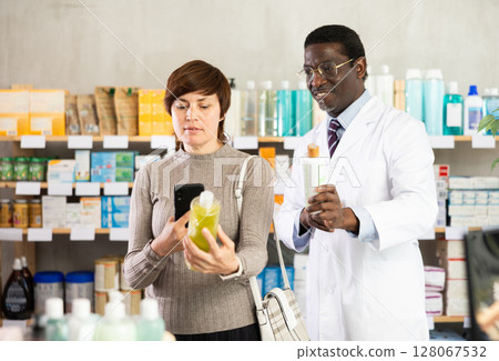 Woman buyer scans shampoo or shower gel qr code with pharmacist Woman buyer scans shampoo or shower gel qr code with pharmacist 128067532