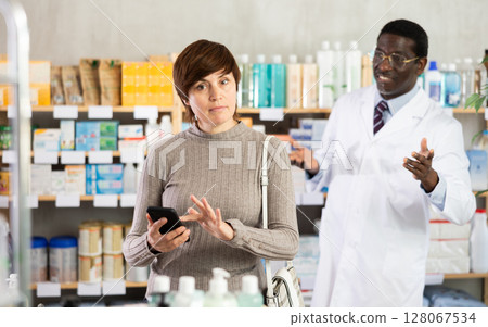 Woman with phone chooses medicines with help of pharmacist 128067534
