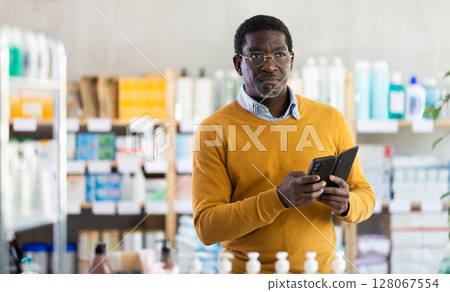 Middle-aged man checking list of medications on phone in drugstore 128067554