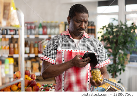 African man customer holds jar of canned olives in hand, scans QR code on product label African man customer holds jar of canned olives in hand, scans QR code on product label 128067563