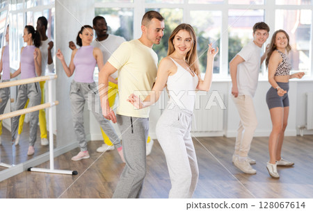 Group of young active multinational people dancing twist or rock and roll dance in dance hall during class 128067614
