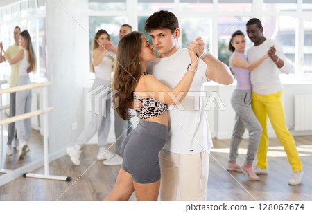 Group of young multiethnic active people in pair dancing social dance movements in studio Group of young multiethnic active people in pair dancing social dance movements in studio 128067674