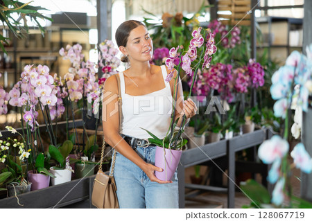 Girl walks through exhibition of ornamental plants, examines orchid in showcase 128067719