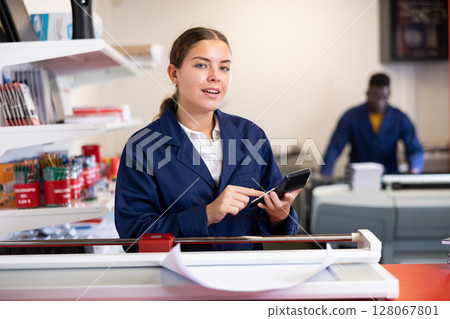 Happy young female in uniform calculates the cost of notepads and sheets in the typography 128067801