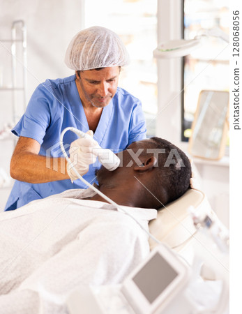 Cosmetologist performing facial cryotherapy procedure on african american Cosmetologist performing facial cryotherapy procedure on african american 128068056