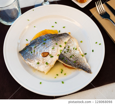 There is large piece of baked fish dorado and potato garnish 128068098