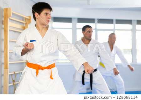 Young judo fighter in kimono practicing punches durig kata with group Young judo fighter in kimono practicing punches durig kata with group 128068114