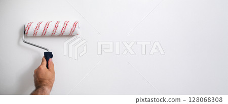 Banner of close up of masculine hand gripping a roller brush, painting a white surface during interior work Banner of close up of masculine hand gripping a roller brush, painting a white surface during interior work 128068308