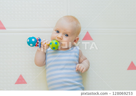 Adorable baby playing with colorful rattles on a soft baby play mat at home. Concept of early development, sensory play, and safe learning environment for infants 128069253