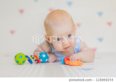 Adorable baby playing with colorful rattles on a soft baby play mat at home. Concept of early development, sensory play, and safe learning environment for infants 128069254