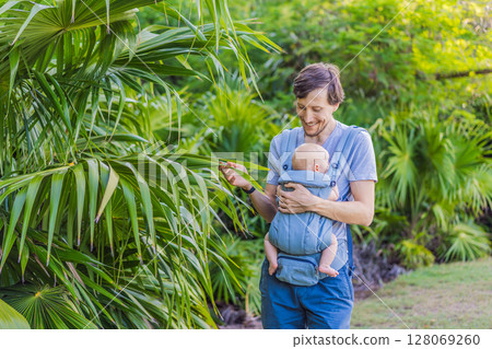 Young father walks in nature with his baby son nestled close in a parent-facing ergonomic baby carrier. Bonding, warmth, and modern parenting concept in a peaceful outdoor setting Young father walks in nature with his baby son nestled close in a parent-facing ergonomic baby carrier. Bonding, warmth, and modern parenting concept in a peaceful outdoor setting 128069260