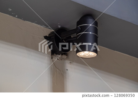 Black cylindrical LED spotlight fixture mounted on a wall emitting bright white light Black cylindrical LED spotlight fixture mounted on a wall emitting bright white light 128069350