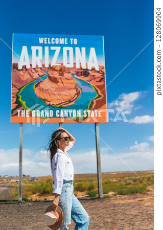 Beautiful woman on her trip to the USA on the background of Welcome to Arizona State border sign right in the Paje Canyon, USA 128069904