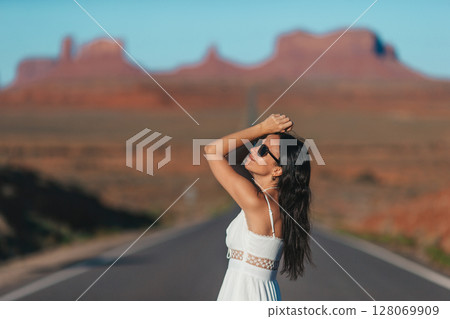 Happy young woman in white dress on the famous road to Monument Valley in Utah. Amazing view of the Monument valley. 128069909