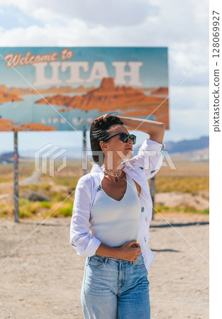 Beautiful woman on her trip by the car. Welcome to Utah road sign. Large welcome sign greets travels in Monument Valley, Utah 128069927