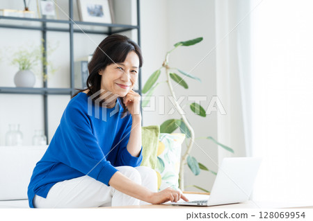 A middle-aged housewife using a computer in the living room A middle-aged housewife using a computer in the living room 128069954