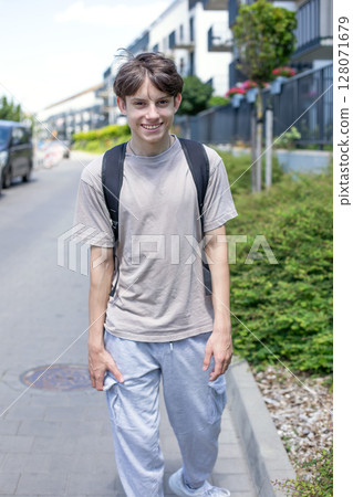 Cheerful cute teenage boy with a backpack walking down the street in sweatpants and a T-shirt 128071679