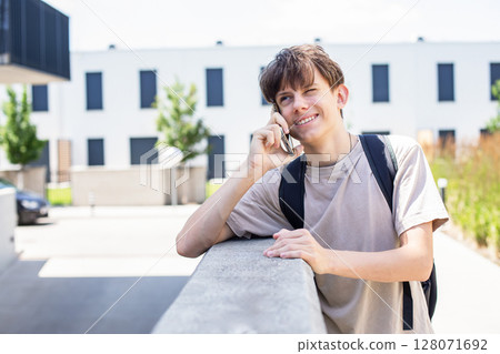 teenage boy with a backpack on his shoulders cheerfully talking on the phone outside on a sunny day teenage boy with a backpack on his shoulders cheerfully talking on the phone outside on a sunny day 128071692