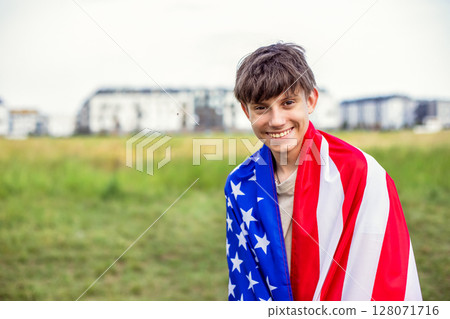Happy teenage boy with American flag on shoulders in field outside city Happy teenage boy with American flag on shoulders in field outside city 128071716