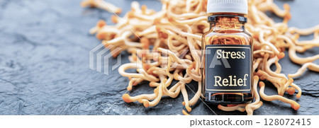 Brown glass bottle with white cap labeled stress relief resting near cordyceps mushrooms on dark textured surface, highlighting natural wellness supplement concept Brown glass bottle with white cap labeled stress relief resting near cordyceps mushrooms on dark textured surface, highlighting natural wellness supplement concept 128072415