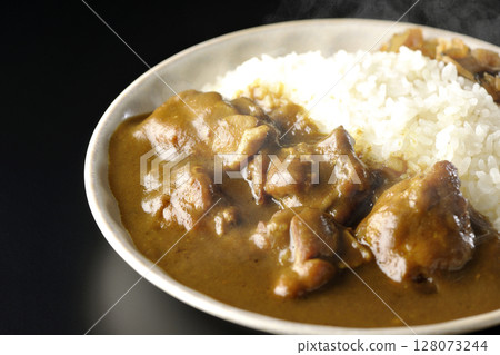 Hot chicken curry with large chunks of chicken photographed against a black background 128073244