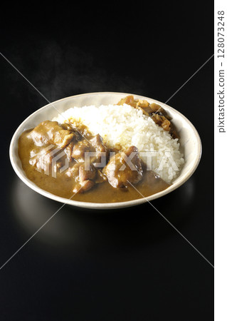 Hot chicken curry with large chunks of chicken photographed against a black background 128073248