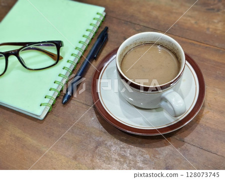 Coffee cup and notebook and pen with glasses on wooden table background Coffee cup and notebook and pen with glasses on wooden table background 128073745