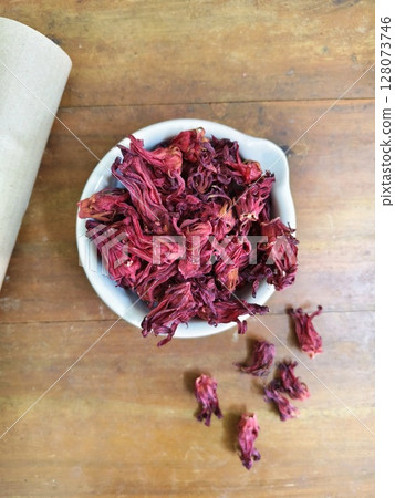 Close up of dry Roselle flower, Jamaica sorrel, Rozelle or hibiscus sabdariffa, in white bowl with old brown wood as background. Close up of dry Roselle flower, Jamaica sorrel, Rozelle or hibiscus sabdariffa, in white bowl with old brown wood as background. 128073746