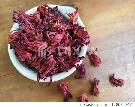 Close up of dry Roselle flower, Jamaica sorrel, Rozelle or hibiscus sabdariffa, in white bowl with old brown wood as background. 128073747