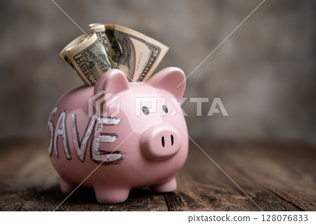 Pink piggy bank and money with banknotes on a wooden table and blue background. Copy space for text. 128076833
