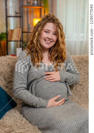 Pregnant young woman laughing at home gently touching belly joyful mood positive happy expression 128077040