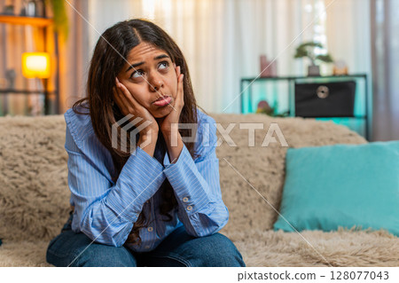 Indian woman feeling heartbroken after breakup with sad emotional face and low energy on home sofa 128077043