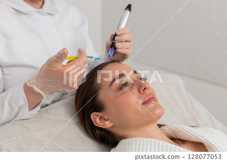 Trichologist doing woman hair regeneration procedure, dermapen microneedling, vitamin injections Trichologist doing woman hair regeneration procedure, dermapen microneedling, vitamin injections 128077053
