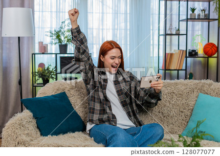 Woman sits on sofa playing mobile game excitedly tapping screen celebrating fun victory and success Woman sits on sofa playing mobile game excitedly tapping screen celebrating fun victory and success 128077077