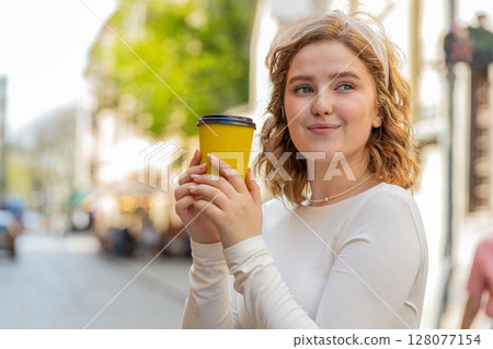 Happy young woman enjoying drinking morning coffee hot drink relaxing taking a break in city street 128077154