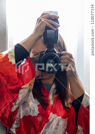 A woman in a red kimono is taking a selfie with a camera A woman in a red kimono is taking a selfie with a camera 128077334