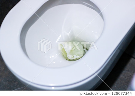 A white toilet featuring a green object resting inside it A white toilet featuring a green object resting inside it 128077344