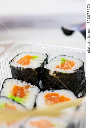 Close up of delicious sushi rolls in a container with chopsticks 128077370