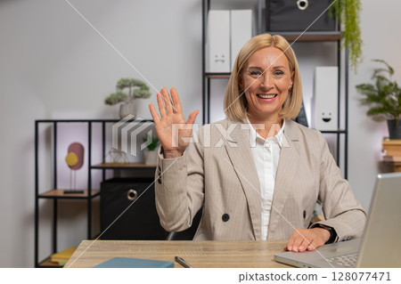 Portrait of mature businesswoman in suit looking at camera after using laptop at home office desk Portrait of mature businesswoman in suit looking at camera after using laptop at home office desk 128077471