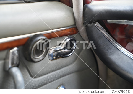 The inner door handles of a vintage car are captured in a clean view, reflecting the classic design and preserved components that represent the simplicity and authenticity of vintage cars. The inner door handles of a vintage car are captured in a clean view, reflecting the classic design and preserved components that represent the simplicity and authenticity of vintage cars. 128079048