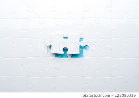 Concept for problem-solving, teamwork, solutions, or missing connections. White jigsaw puzzle on a vibrant blue background with one missing piece. Minimalist composition with copy space. Concept for problem-solving, teamwork, solutions, or missing connections. White jigsaw puzzle on a vibrant blue background with one missing piece. Minimalist composition with copy space. 128080339